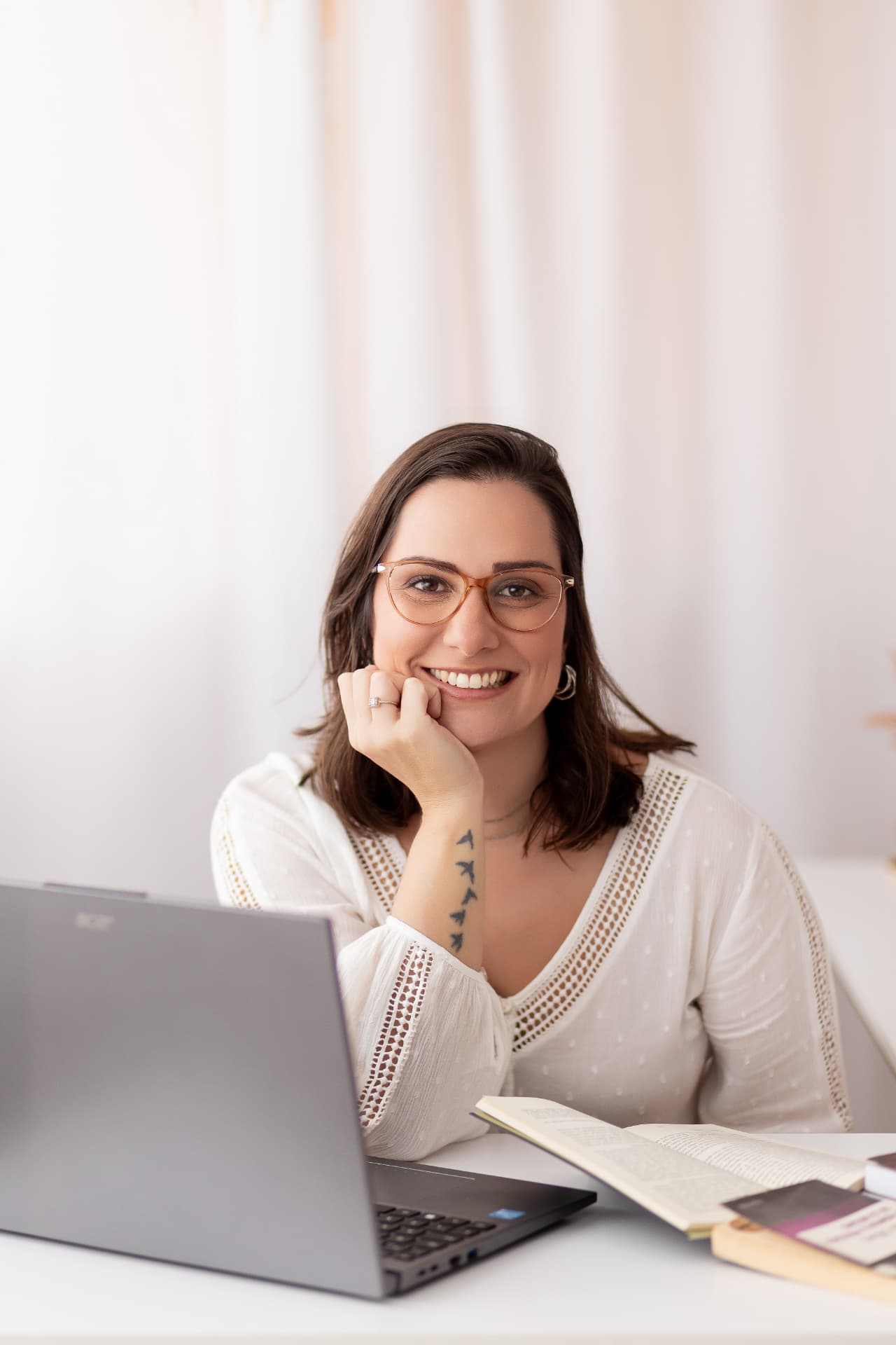 Mariana Lanza Guarnieri sorrindo, sentada à mesa com um notebook e livros